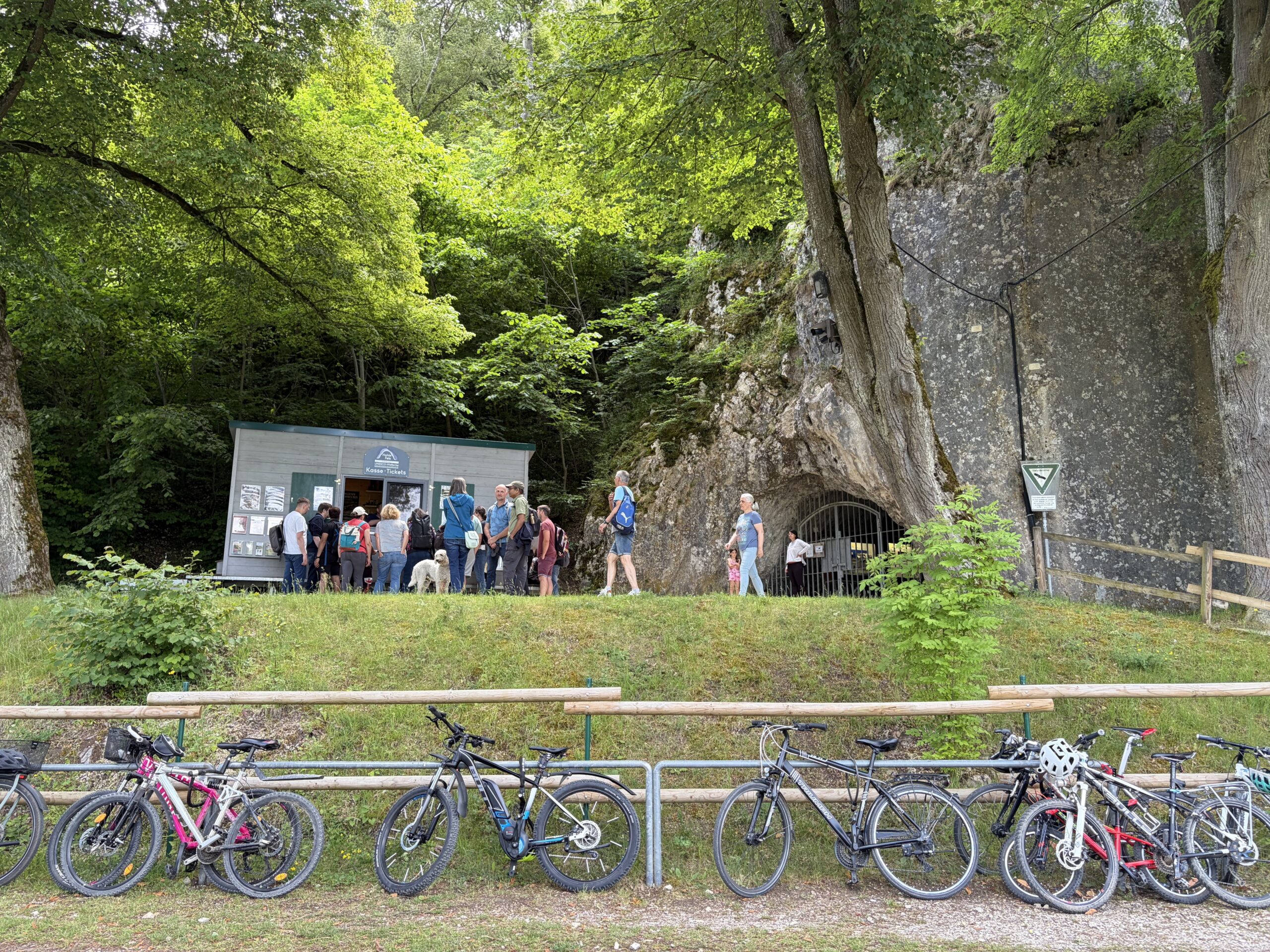 Eine Gruppe von Menschen vor einem Ticketcontainer neben dem Hohle Fels-Eingang. Im Vordergrund sind Fährräder an einen Zaun angelehnt.